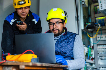 Engineers performing maintenance in a wind turbine tower using a laptop and tools