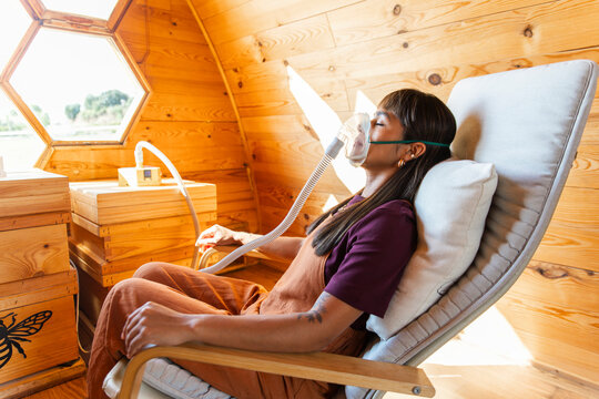 Person inhaling bee air with breathing mask for apitherapy in wooden cabin