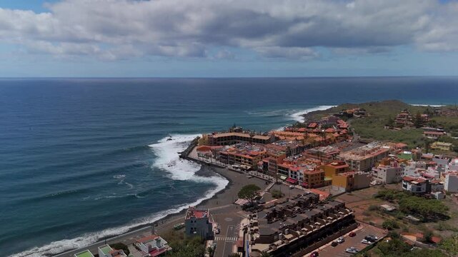 Wide aerial drone shot soaring above the colorful coastal town of La Calera, revealing the black sand beach and deep blue Atlantic Ocean in Valle Gran Rey, La Gomera.