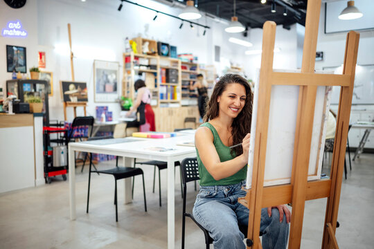 Smiling artist painting on canvas at art studio indoors
