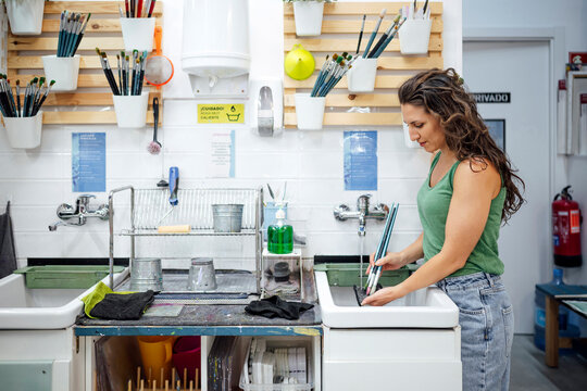 Artist cleaning paintbrushes at studio sink during creative workshop