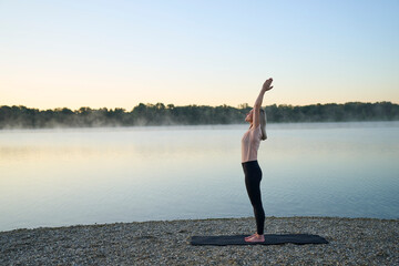 Person practicing yoga at sunrise by a lake in nature outdoors