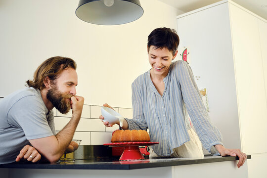 Man with woman decorating cake in kitchen at home
