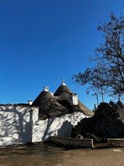 Trullo Architecture: A picturesque scene of traditional Trullo architecture bathed in the bright sunlight, with their characteristic conical roofs reaching towards a vibrant blue sky.