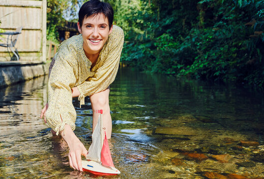 Smiling woman playing with boat in stream