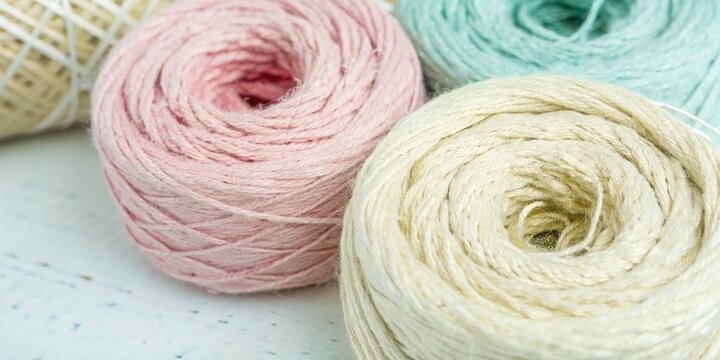 Close-up of three tightly wound balls of natural fiber yarn in soft pastel colors: pink, cream, and mint green. Use for craft, textile, and hobby blogs/sites.