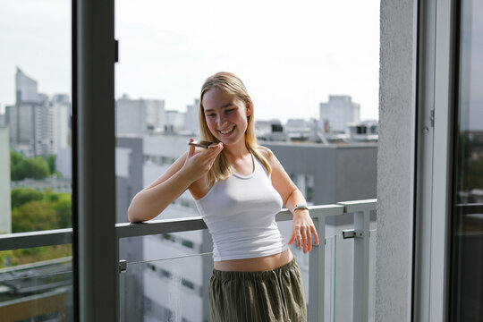 Smiling woman on balcony making phone call outdoors in urban setting