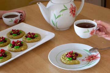 A girl's hand and a child's hand holding a cup of tea against a background of pistachio cookies.