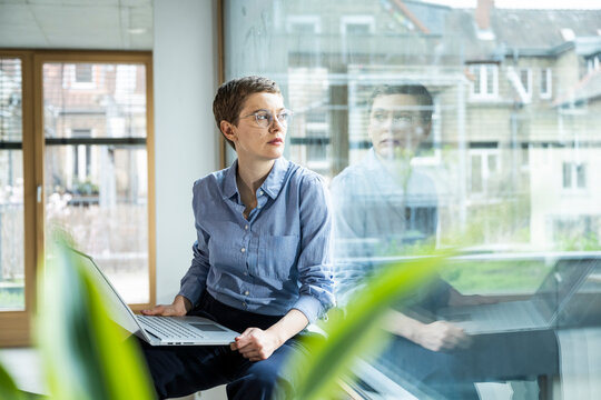Businesswoman in office with laptop looking away thoughtfully