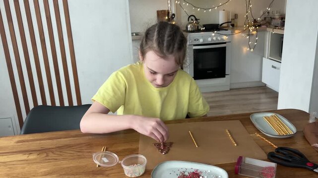 Little girl decorating homemade chocolate Christmas tree cookies in the kitchen. Festive baking and childhood fun