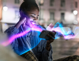 Smiling woman using mobile phone with glowing effects at night outdoors