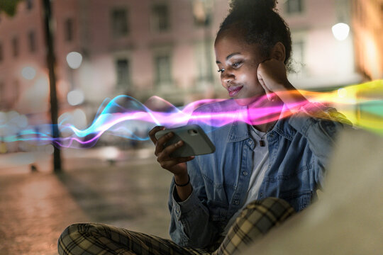 Smiling woman using mobile phone with glowing effects at night outdoors - Powered by Adobe
