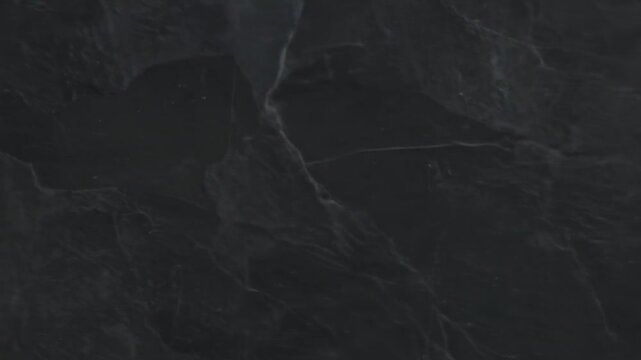 Close-up of dark grey stone with surface texture, veining, and natural patterns