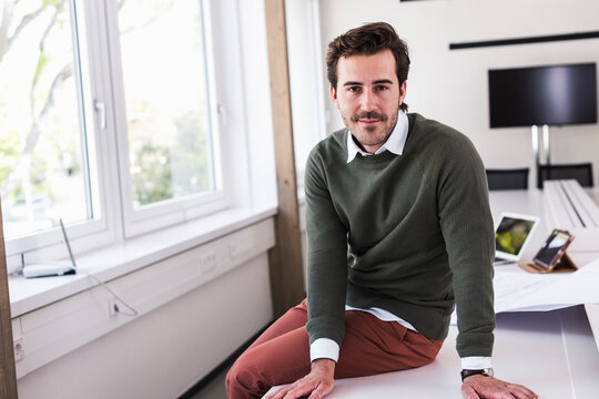 Architect sitting on desk in modern office with plans and tablet