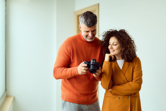 Two Friends Explore a Camera Together in a Bright Modern Workspace with Warm Orange Tones