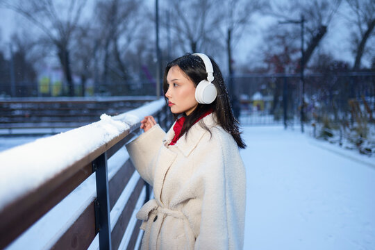 Woman wearing white coat and headphones outdoors in snowy park