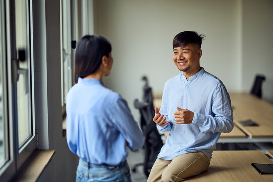 Asian Man and Woman in Office: Friendly Conversation Between Coworkers in Modern Workspace - Powered by Adobe