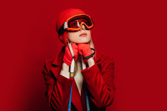 Stylish person in red coat and ski mask posing with ski poles