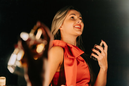 Smiling woman in red dress applies perfume in front of mirror
