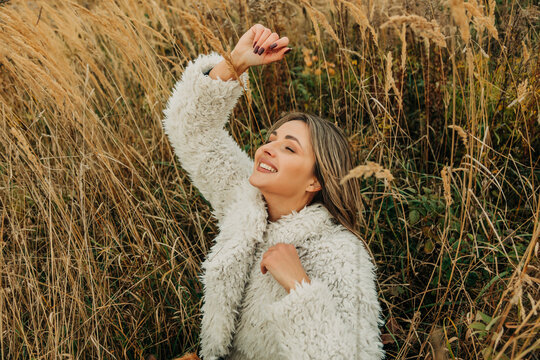 Smiling woman relaxing in high dry grass outdoors in autumn wearing white jacket