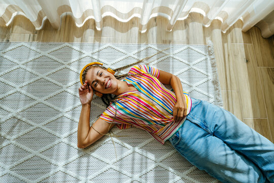 Happy young woman listening to music and relaxing on carpet at home