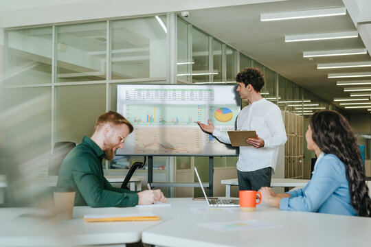 Business colleagues discussing strategy in a coworking office with a screen displaying graphs