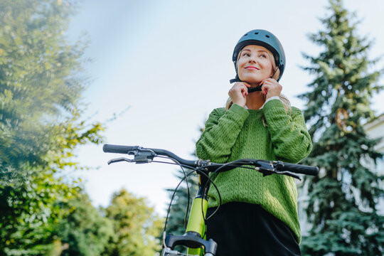 Woman in business wear fastening helmet while commuting by bicycle outdoors