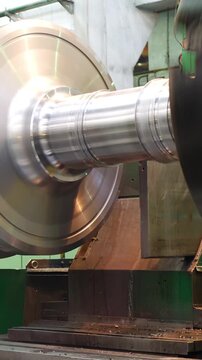 Steel billet turns in lathe while machine forms turbine rotor. Process part of wind power equipment upgrade during overhaul at sustainable energy production facility