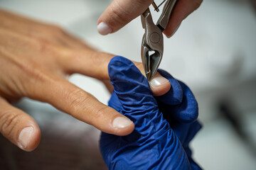 Close-up of nail technician cutting cuticles with professional clippers during manicure procedure