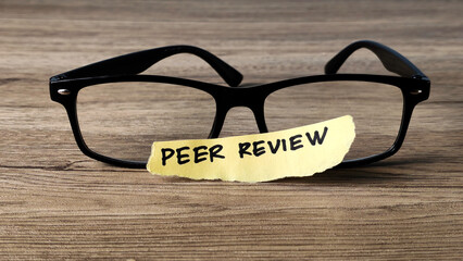 Peer Review concept with a handwritten note placed on reading glasses on a wooden desk, symbolizing...