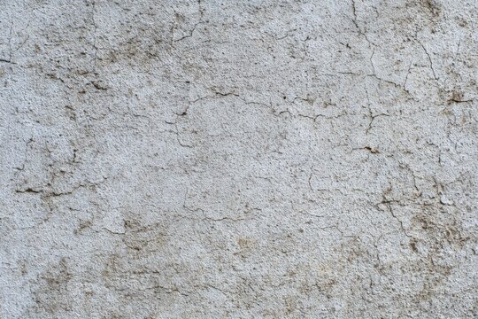 Textured surface a rough light gray material with numerous small cracks and dark spots scattered across it