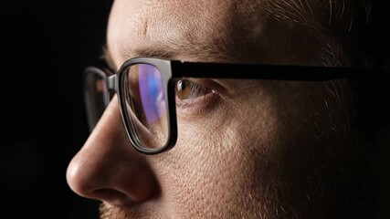 Close-up profile view of a man wearing glasses, with reflections visible in the lenses against a dark background, highlighting facial features and eyewear detail - Powered by Adobe