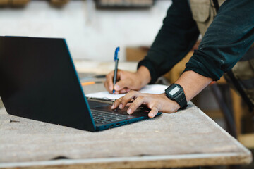 Close-up of a carpenter using a laptop at a workbench. Close up of a man using a laptop in the carpentry shop