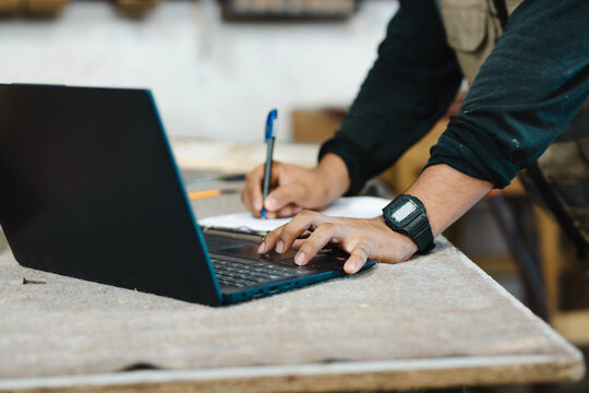 Close-up of a carpenter using a laptop at a workbench. Close up of a man using a laptop in the carpentry shop - Powered by Adobe