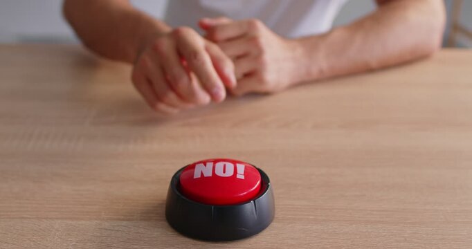 Close-up of a red no button on a wooden desk, with hands in the background, signaling refusal and a decisive stop. A firm stop and refusal. Reject, deny, decision, veto, prohibition, boundary.