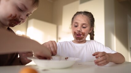 Fototapeta premium baby boy and girl eat chocolate. dirty little baby kids in the kitchen eating chocolate in the morning. happy family eating sweets kid dream concept. baby dirty sweet face eating chocolate cocoa