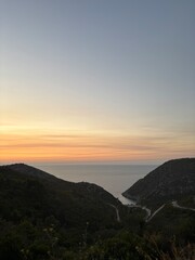 Sunset over a traditional Greek island with whitewashed houses, blue domed roofs, and narrow stone streets. Warm golden and orange light reflecting on the Aegean Sea, creating a peaceful and romantic 