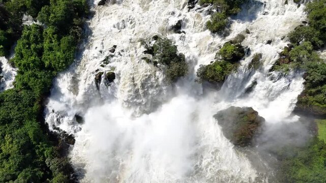 Drone top view of Binga Falls, Angola, capturing the raw power of the waterfall as it crashes over rocks, creating mist and foam in the heart of the jungle