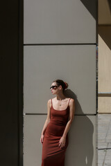 Modern young fashionable woman in basic cotton brown camisole dress. Spring summer clothes on a city street. Trendy women's clothing, street fashion trend.	