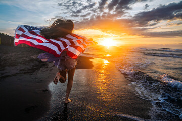 Young woman holding national American flag walking ocean beach. America Independence Day concept