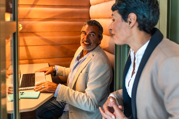 Coworkers collaborating in modern office booth using laptop