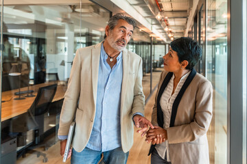 Business colleagues walking and discussing work in office corridor