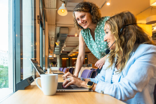 Coworkers collaborating and smiling while working with laptops and headsets