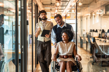 Diverse business colleagues pushing woman in wheelchair at office