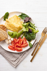 French omelet, avocado, tomatoes, salad, cheese, and bread toast on plate. Healthy breakfast on white table, angle view.