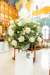 Elegant floral arrangement stands in a church filled with colorful decorations, showcasing white roses and greenery