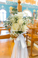 White rose bouquet with baby's breath decorates a wooden chair in a church setting during a wedding...