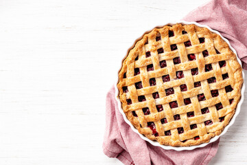 Classic American raspberry pie in ceramic pan on napkin on white wooden background.