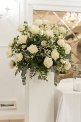 Elegant white rose bouquet displayed in a modern vase at a wedding reception venue in the evening