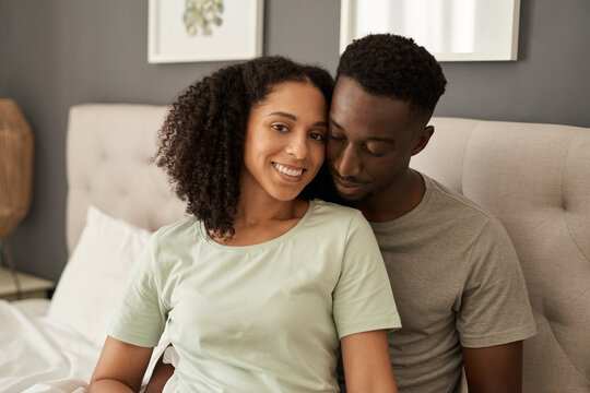 Smiling young multiracial couple sitting in their bedroom in the morning